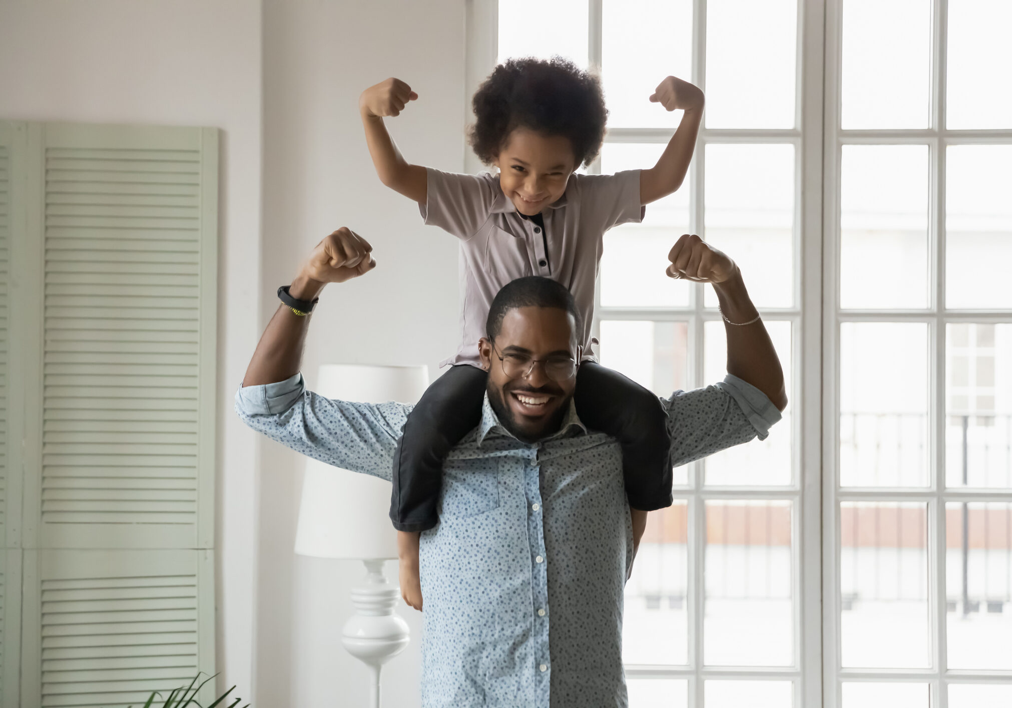 Small son sit on strong dad shoulders showing biceps. African family enjoy activity games at home, healthy fit lifestyle, two superheroes, vitamins for adults and children ad, happy Father Day concept